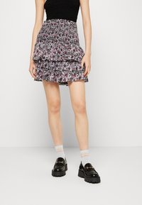 Gonna mini nera a fiori con tre strati arricciati, con vita smock e sfondo scuro. Indossata con mocassini neri chunk e calzini a fantasia.