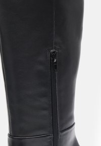 Schwarze Lederstiefel in kniehohem Design mit einem seitlichen Reißverschluss, glatter Oberfläche und gestepptem Designdetail entlang des Schafts. Elegante Form und Verarbeitung.