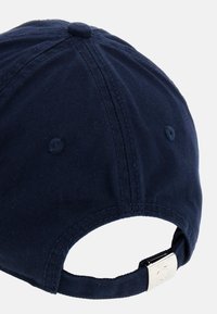 Gorra azul marino hecha de tejido texturizado, con visera curva y correa ajustable con una hebilla de metal en la parte posterior. Detalles de costura visibles.
