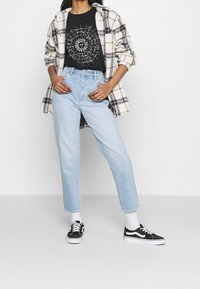 Camisa de franela a cuadros, camiseta gráfica negra, jeans de pierna recta azul claro, zapatillas negras con detalles blancos y calcetines blancos.
