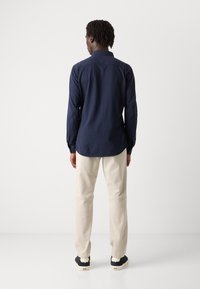 Marineblauw overhemd met lange mouwen en een button-down kraag, gecombineerd met beige broek en marineblauwe sneakers. Gladde stof met een getailleerde pasvorm.