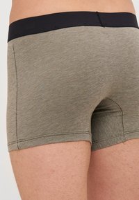 Männerboxershorts aus einem strukturierten, olivgrünen Stoff. Verfügt über einen schwarzen elastischen Bund und einen körpernahen Schnitt. Die Nähte sind für Strapazierfähigkeit genäht.
