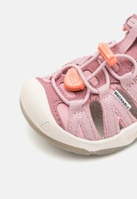 Pink washable sandal with a textured suede upper, elastic straps, and rubber sole. Features a prominent tightening mechanism and ventilation holes.