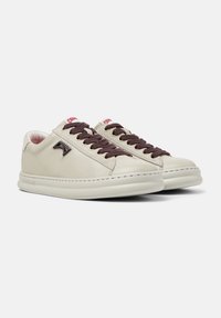Sneaker in pelle beige con lacci marroni scuri, suola bianca e dettagli del logo ben visibili di lato. Interno con rivestimento morbido.