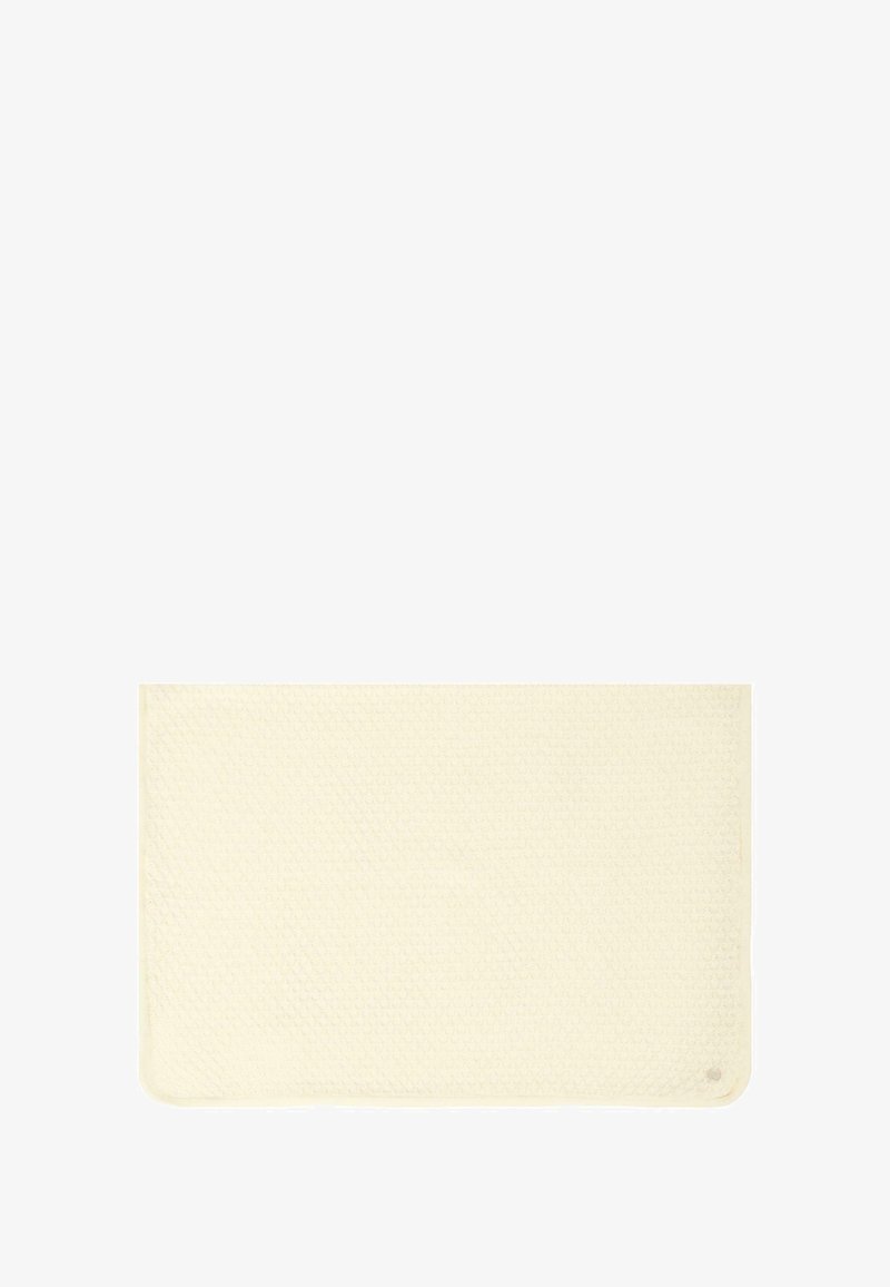 Prostokątny dywanik łazienkowy w kolorze kremowym, teksturowana powierzchnia z wzorem w komórki, wykończone krawędzie oraz małe logo w jednym z rogów.