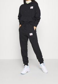 Zwarte hoodie en joggingbroek set van een katoenmengsel, met witte logopatches. De hoodie heeft een trekkoord en de broek een elastische tailleband.