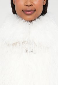 Bela umetna krzna ovratnik s sleek obliko. Ima sijoč srebrn zaponko na sredini, kar ustvarja mehko, teksturirano podobo.