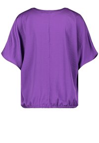 Lila batwing-topp med rundad halsringning och elastisk nederkant; tillverkad av ett mjukt, lätt tyg med en lätt lyster.