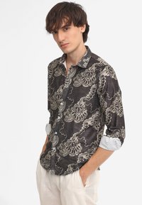 Camicia a fantasia nera e crema con un design floreale, dotata di colletto button-down, maniche lunghe e polsini bianchi a fantasia in contrasto.