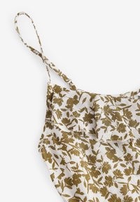 Camisole floral avec bretelles ajustables. Le matériau présente une base blanche avec un motif de fleurs vert olive et des détails froncés le long du haut.