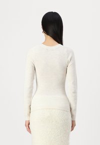 Suéter de punto beige claro con mangas largas y un escote redondeado, presenta un diseño ajustado y una textura suave.