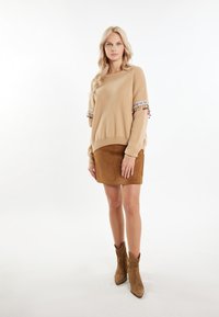 Beige gebreide trui met kleurrijke, franjes aan de mouwen. Gecombineerd met een bruin suède minirok en bruin suède enkellaarsjes.