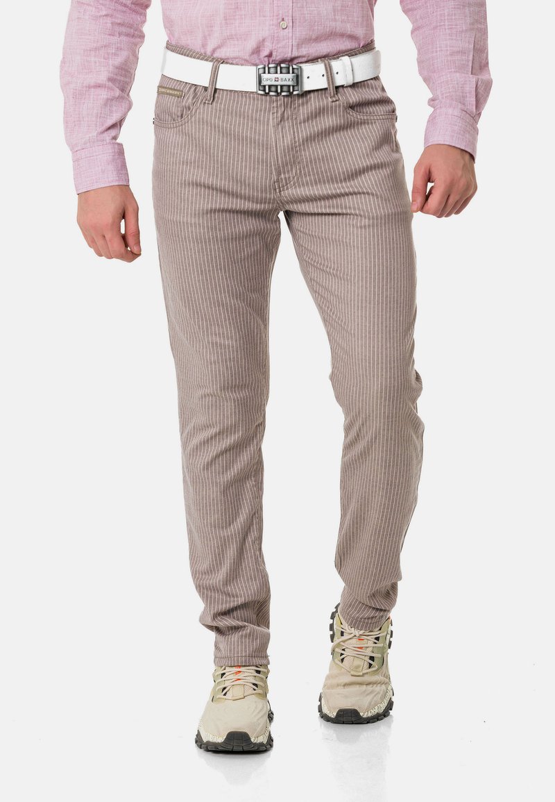 Beige gestreifte Hosen aus einer Baumwollmischung, mit einem Slim-Fit-Design, einem weißen Gürtel und kombiniert mit hellen Sportschuhen.