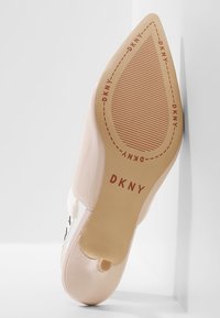 Escarpin rose clair avec une finition brillante. Présente une pointe aiguë et une semelle texturée. Logo "DKNY" estampé sur le dessous.