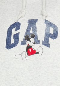 Felpa grigia con audace scritta "GAP" in blu navale e un cartone animato di Topolino con pantaloni rossi a pois bianchi e scarpe nere.