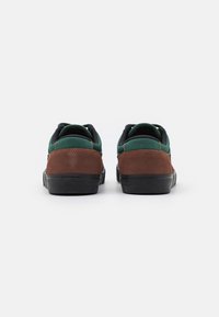 Green and brown sneakers with a suede and canvas upper, black accents, and a textured rubber sole. Rear view shows padded collar and stitching.
