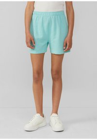 Shorts turquoise texturés avec une taille élastique et des poches latérales, associés à des baskets blanches sur un fond uni.