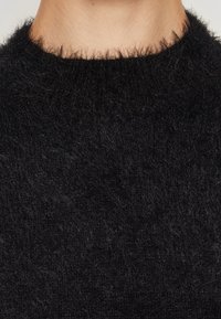 Zbliżenie na szyję i kołnierz czarnego, miękkiego swetra o miękkiej, teksturowanej dzianinie.