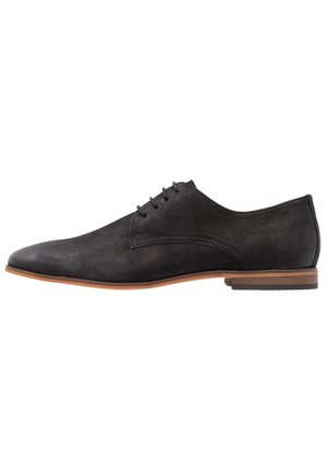 Black suede men's oxford shoe with brown sole and low heel, side view, lace-up closure, smooth rounded toe.