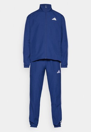 Blauer Trainingsanzug mit einer Reißverschlussjacke mit hohem Kragen, weißen seitlichen Streifen und passenden Hosen mit einem Adidas-Logo. Glatte Stofftextur.