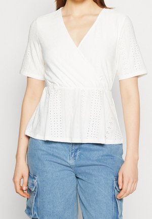 Vrouw draagt een wit wikkelblouse met korte mouwen, oogjesdetails en een elastische taille, gecombineerd met lichtblauwe cargo denim shorts.