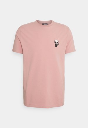 Różowy t-shirt z krótkim rękawem z małą czarno-białą postacią z kreskówki w okularach przeciwsłonecznych na lewej części klatki piersiowej.