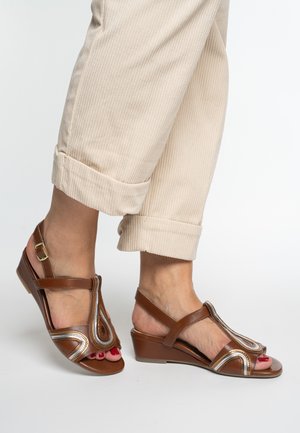Brown leather wedge sandals with an open toe, decorative swirl design featuring metallic accents, and adjustable ankle strap.