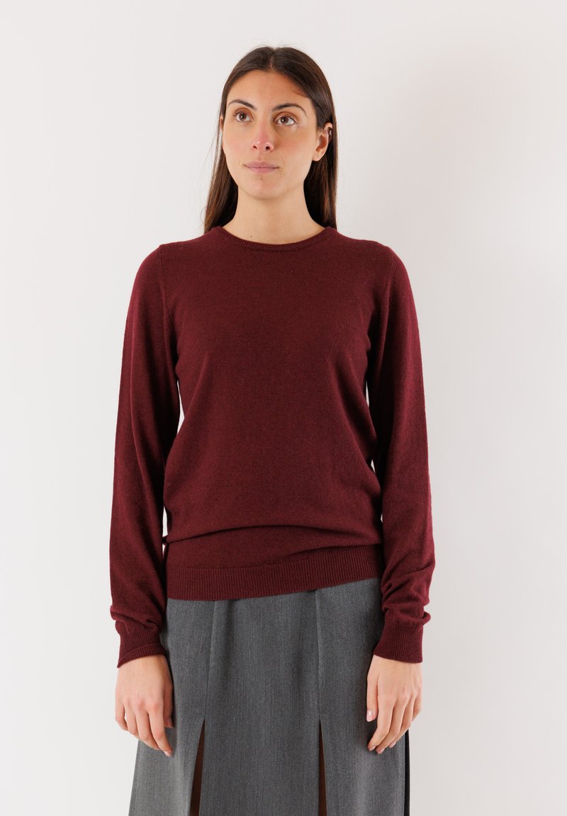 Maglione a maglia bordeaux con maniche lunghe e scollatura rotonda, caratterizzato da una texture morbida e un orlo a coste, abbinato a una gonna grigia.