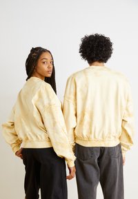 Chaquetas bomber de tie-dye amarillas con puños y dobladillos elásticos, que presentan un corte relajado, bolsillos laterales y un acabado texturizado.