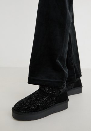 Czarne botki za kostkę z teksturowaną cholewką ozdobioną cyrkoniami oraz grubą gumową podeszwą. Stylizowane z czarnymi aksamitnymi spodniami.