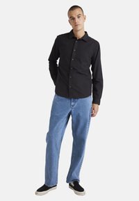 Black long-sleeve shirt with buttons, blue denim jeans, and black slip-on shoes. The shirt has a collar and a relaxed fit.