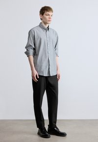 Szürke-fehér csíkos gombos hosszú ujjú ing, fekete nadrággal és fekete cipővel párosítva. Simább anyag, kényelmes szabás.