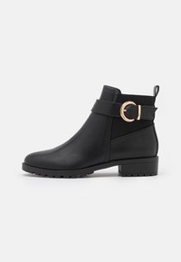 Bottines en cuir noir avec une finition texturée, présentant un accent de boucle sur le côté et une semelle en caoutchouc avec un petit talon carré.