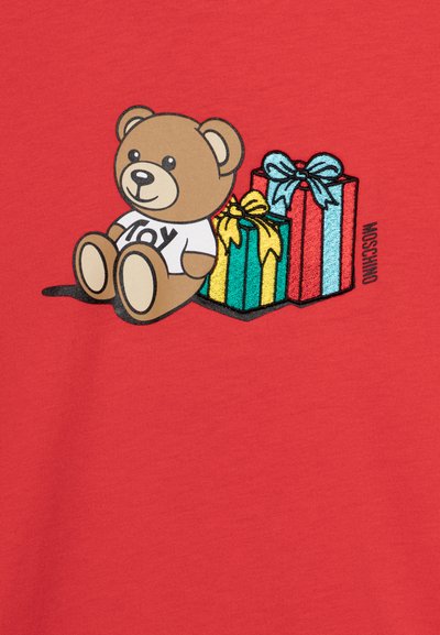 Una tela roja presenta un oso de dibujos animados con la palabra "ALEGRÍA" en su camiseta, sentado junto a dos regalos coloridos envueltos con lazos. El diseño está bordado.