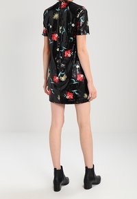 Robe courte noire en sequins avec broderie florale, manches courtes et fermeture éclair au dos. Portée avec des bottines noires. Texture lisse et brillante.