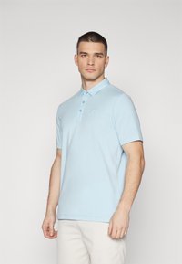 Lyseblå polo skjorte med krage, tre knapper og en liten logo på brystet. Laget av et glatt stoff med korte ermer.