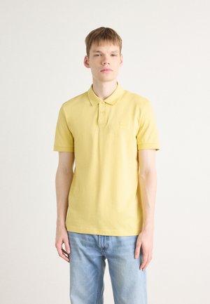 Tricou polo galben din bumbac, cu guler, mâneci scurte și un mic patch cu logo pe piept. Purtați-l cu blugi albaștri.