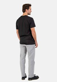 Black cotton t-shirt with short sleeves, paired with light grey pants and black shoes, viewed from the back against a plain background.