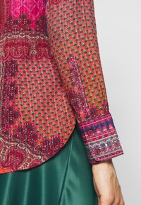 Mehrfarbiges Hemd in Rot und Rosa mit strukturierten Punkten, detaillierten Manschetten mit Knöpfen und einem kontrastierenden Design am Saum.