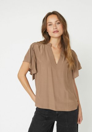 Blusa marrone a V con maniche corte e ampie, con dettagli plissettati sulle spalle e un tessuto morbido e leggero. Abbinata a jeans neri.
