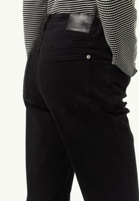 Schwarze Jeans aus Denim mit tailliertem Design. Merkmale sind Gesäßtaschen, ein Lederpatch am Bund und dezente Nähdetails.