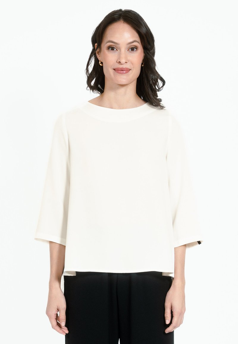 Top color crema, dalla vestibilità morbida, con maniche a tre quarti, collo rotondo e una texture liscia, abbinato a pantaloni neri.