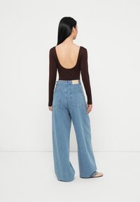 Bodysuit marrón de manga larga con un escote profundo en la parte de la espalda, combinado con unos pantalones vaqueros de mezclilla azul claros de pierna ancha. Los pantalones tienen una etiqueta en la parte de atrás.