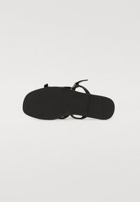 Sandale noire avec une tige en cuir lisse, de fines lanières et une semelle en caoutchouc plat avec un motif texturé pour une meilleure adhérence. Accent en métal doré.