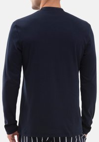 Uomo che indossa una semplice maglietta a maniche lunghe blu navy e pantaloni neri con strisce verticali bianche, mostrato di spalle.