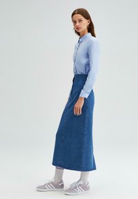 Chemise boutonnée bleu clair, jupe en denim arrivant aux chevilles avec des embellissements en perles, assortie à des baskets grises. Texture douce, coupe décontractée.