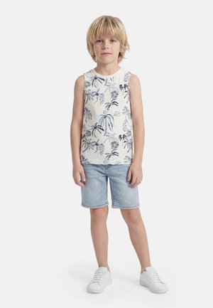 Blond boy standing with hands by sides wearing white sleeveless top with blue tropical print, light denim shorts, and white sneakers.