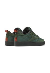 Green suede sneakers with a black rubber sole, featuring orange patterned accents at the heel and purple eyelets for the laces.