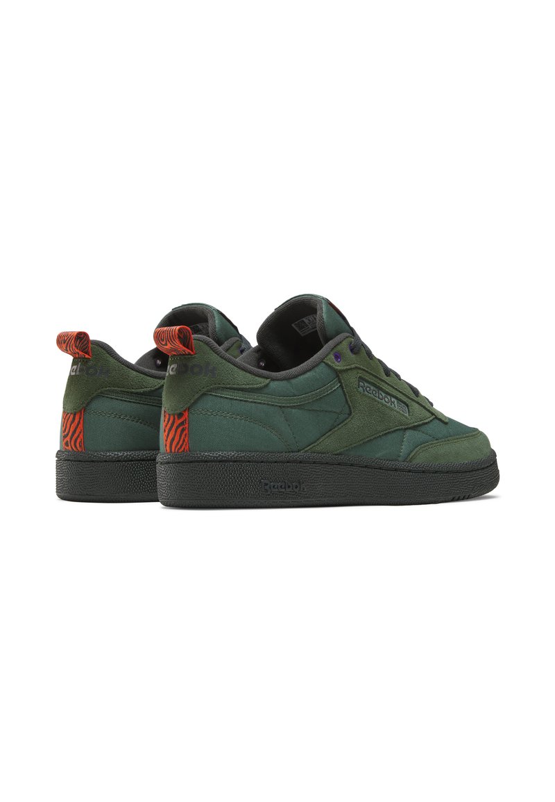 Baskets en daim vert avec une semelle en caoutchouc noir, présentant des accents à motif orange au niveau du talon et des œillets violets pour les lacets.
