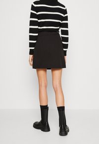 Svart mini kjol med en mjuk textur, parat med en svart och vit randig stickad tröja och knähöga svarta stövlar.